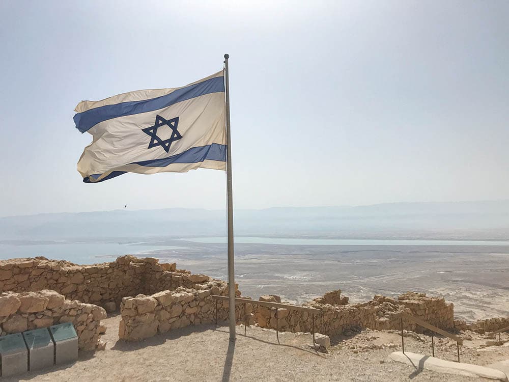 The Israeli flag waves from the hilltop fortress, 
Masada with the Dead Sea in the distance.