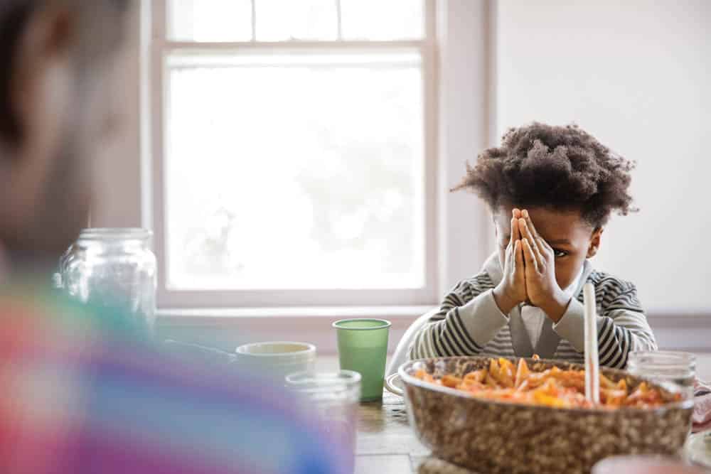 Boy Looking At Father While Praying At Dining Table