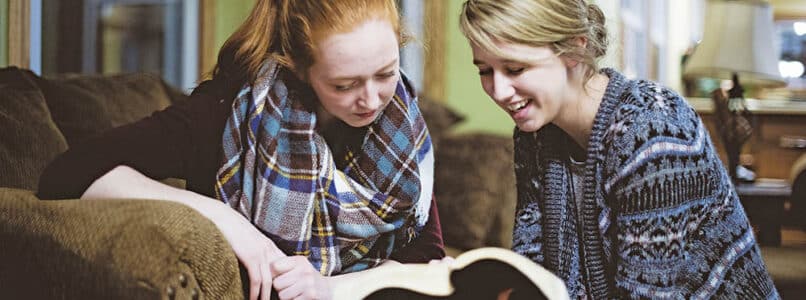 Two young female friends sitting on the couch and discussing the Bible