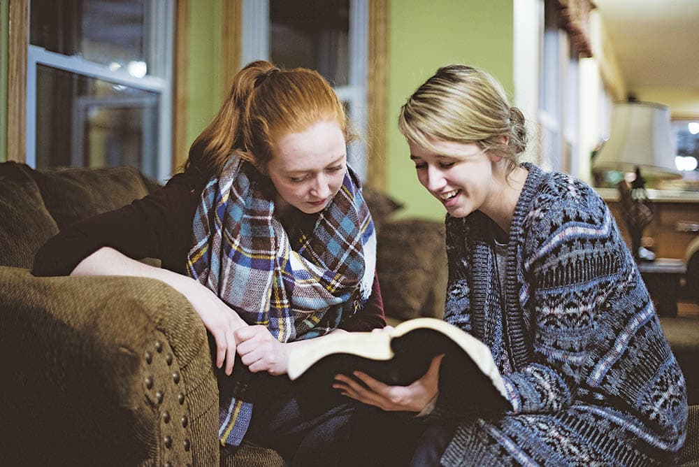 Two young female friends sitting on the couch and discussing the Bible